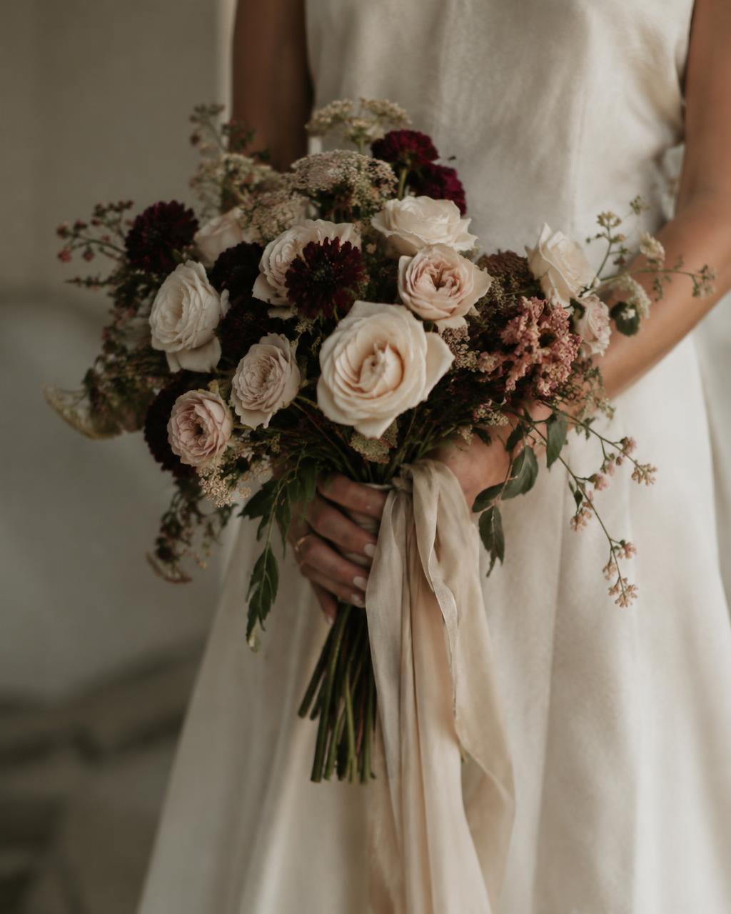A bride holding a garden bouquet of cream roses and burgundy dahlias